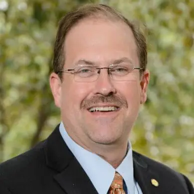 A man with glasses and a beard wearing a suit.