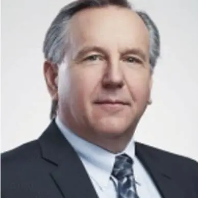 A man in suit and tie with grey hair.
